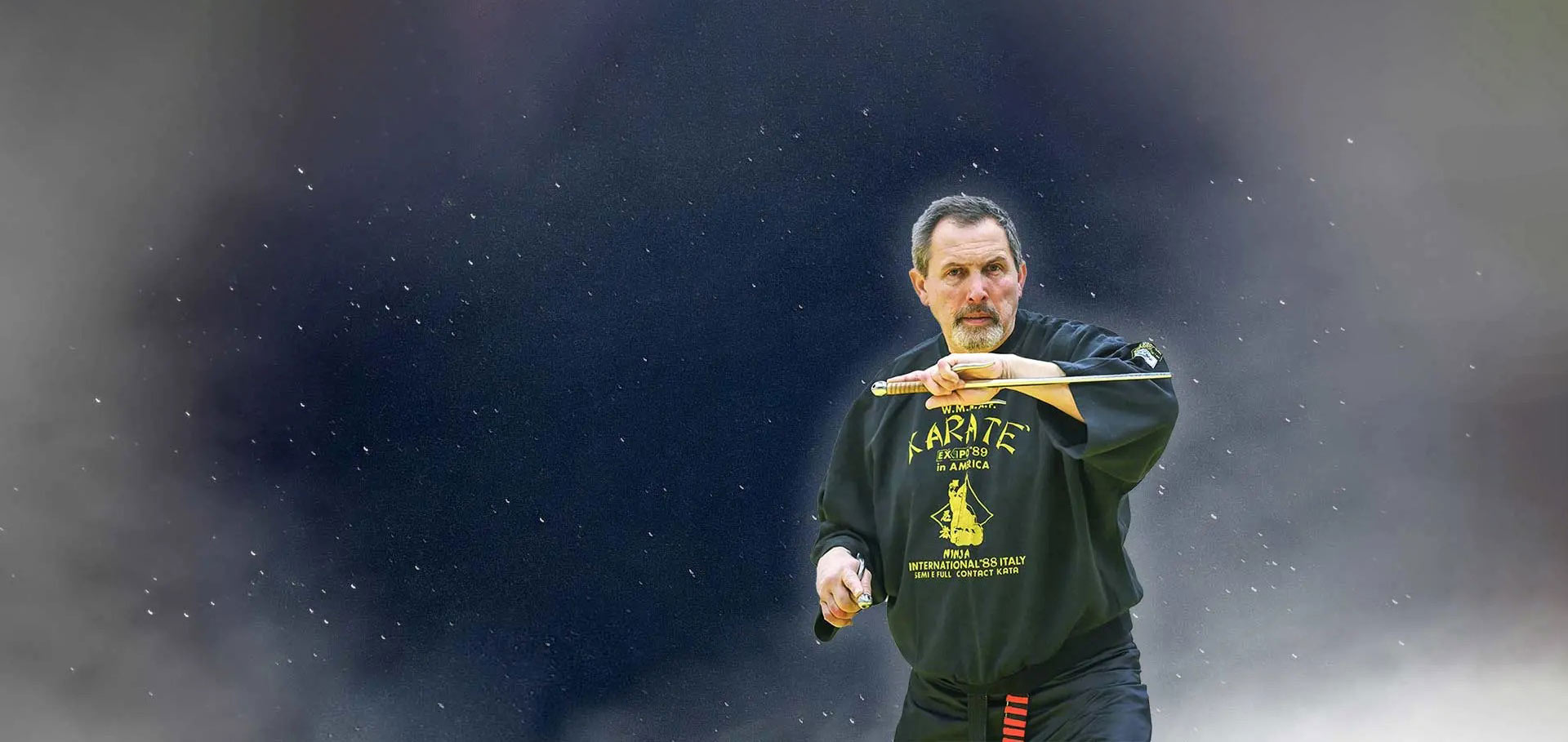 David Stainko u tamnoj majici drži tradicionalno oružje ispred sebe